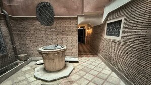 Un patio con una fuente de piedra central, paredes de ladrillo y un piso con diseño de ajedrez.