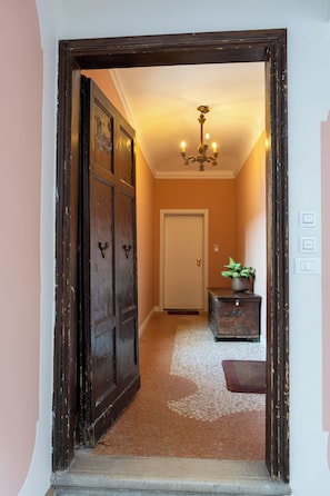 A hallway with a wooden door, a chandelier, a small table with a plant, and a white door at the end. - Historic Palace with Private Terrace | Grand Views over Campo Santo Stefano (Venezia)