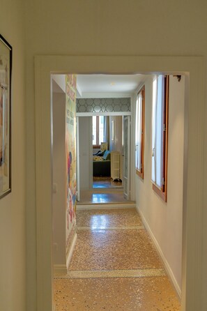 A hallway with a polished floor, a bed in the background, and a radiator. - Historic Palace with Private Terrace | Grand Views over Campo Santo Stefano (Venezia)