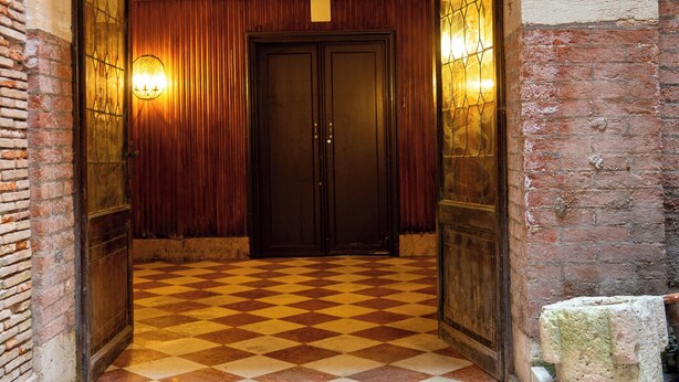 Una entrada en arco con piso a cuadros, una puerta de madera y una pared con un accesorio de luz.