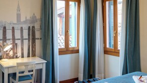 Una habitación con cama, escritorio, silla, ventana con cortinas y un candelabro.