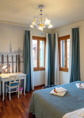 A room with a bed, a desk, a chair, a window with curtains, and a chandelier. - Historic Palace with Private Terrace | Grand Views over Campo Santo Stefano (Venezia)