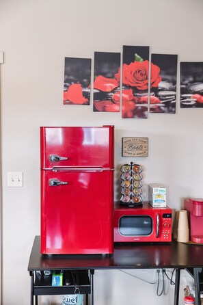 Una cocina con un refrigerador rojo, un microondas y una cafetera sobre una encimera negra.