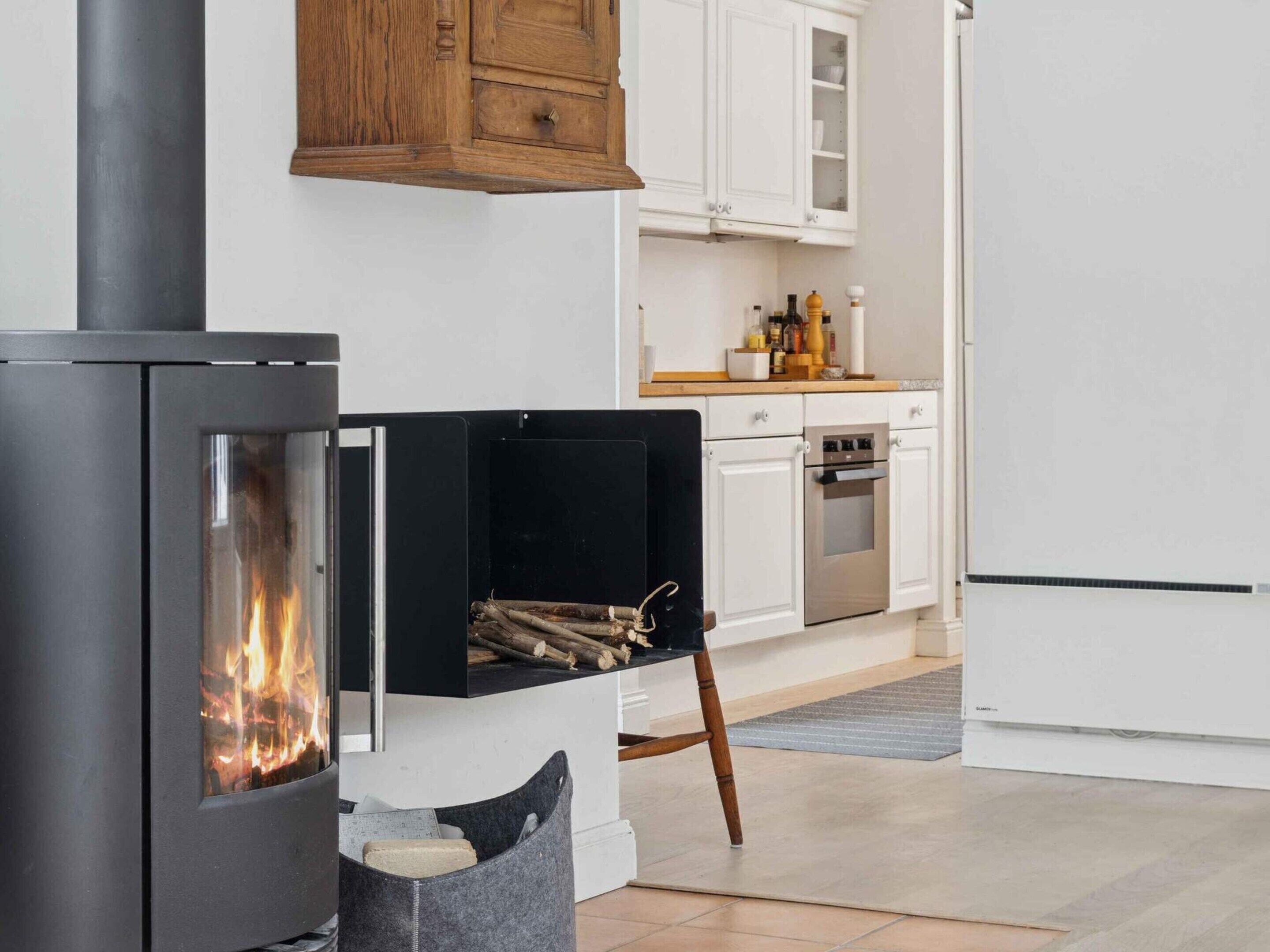 A modern kitchen with a wood-burning stove, white cabinets, and a stainless steel oven.