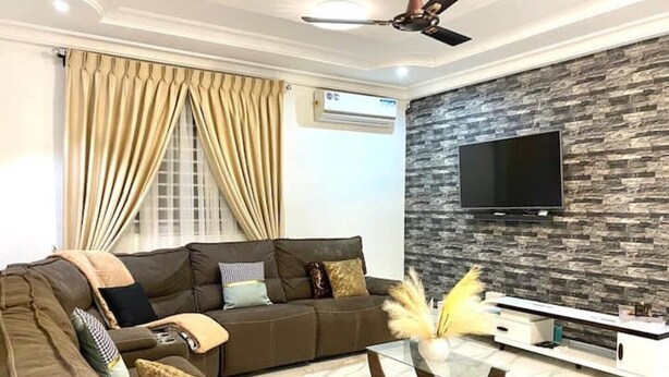 Una sala de estar moderna con un sofá, una mesa de centro de vidrio, un televisor de pantalla plana montado en una pared con textura de piedra y un ventilador de techo.