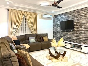 Uma sala de estar moderna com sofá, mesa de centro de vidro, TV de tela plana fixada em parede com textura de pedra e ventilador de teto.
