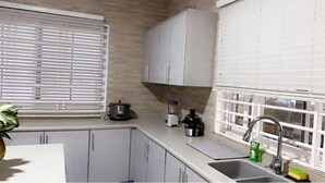 Una cocina con armarios blancos, un lavamanos, una estufa y una ventana con persianas.