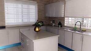 Una cocina moderna con armarios blancos, una isla central y un ventanal con persianas.