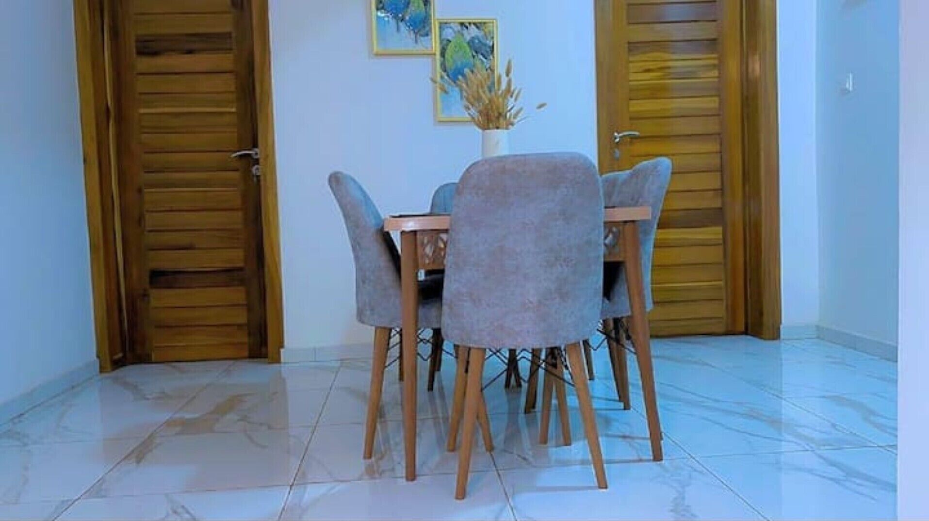 A dining area with a table and chairs, wooden doors, and a vase with dried plants on the wall.