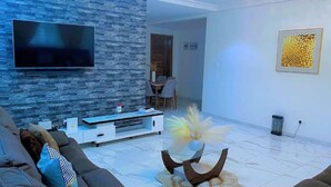 Una sala de estar moderna con una pared de piedra, un televisor de pantalla plana, un comedor y una planta decorativa.