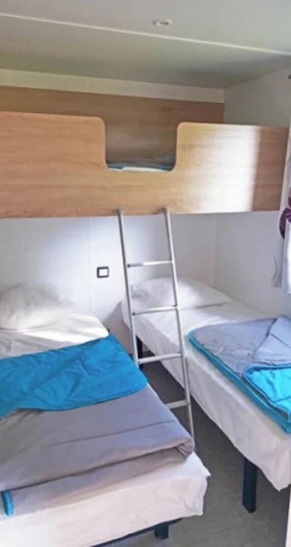 A bunk bed room with a ladder, white bedding, and a wooden headboard.