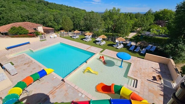 Una piscina con toboganes, tumbonas y un área cercada con sombrillas.