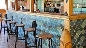 A bar area with wooden stools, a counter with bottles, and a decorative wooden sculpture. - ZEcamping 3* pataugeoire piscine chalet 31m2 6 pers (Saint-Projet)