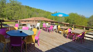 Una terraza de madera con mobiliario exterior, incluyendo mesas y sillas, y un paraguas azul con la marca 'Nestle'.