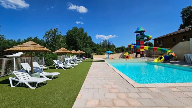 Una piscina con tobogán, tumbonas y sombrillas.