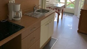 Une cuisine équipée d’une cuisinière, d’une machine à café, d’un évier et de placards. Un escalier mène à un balcon où se trouvent une table et des chaises.