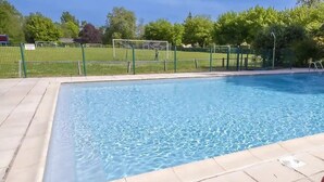 Une piscine rectangulaire bordée de carreaux, entourée d’une clôture verte, avec des arbres en arrière-plan.