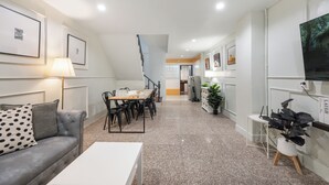 Una sala de estar moderna con sofá, mesa de comedor y sillas, una escalera y un pasillo que conduce a una cocina.