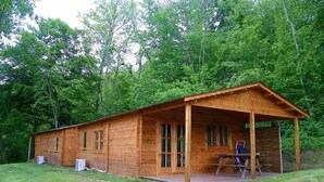 A wooden cabin with a porch, a picnic table, and two air conditioning units.