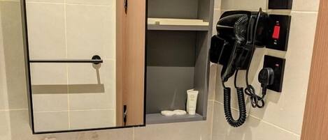 Un baño con lavamanos blanco, espejo, toallero, secador de pelo y estante con artículos de aseo.