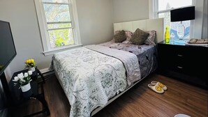 A bedroom with a bed, a dresser, a TV, and a window.