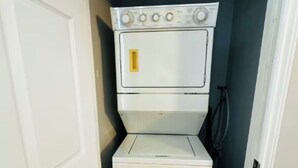 A compact laundry room with a stacked washer and dryer, a small window, and a door leading to another room.