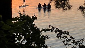 Un atardecer sobre un lago tranquilo con gente practicando paddleboard y sentada en un bote.