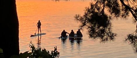 A sunset over a calm lake with people paddleboarding and sitting in a boat.