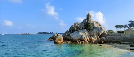 Un paysage côtier caractérisé par une formation rocheuse imposante et un petit bâtiment situé au sommet, d’où l’on a une vue sur la mer.