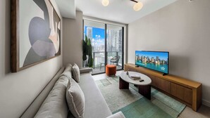 Un salon moderne avec un canapé, un téléviseur et une vue sur le paysage urbain grâce à de grandes fenêtres.