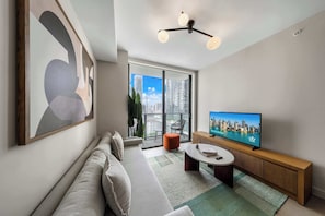 Ein modernes Wohnzimmer mit einer Couch, einem Fernseher und Blick auf die Stadt durch große Fenster.