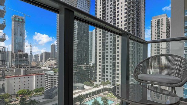 Un balcon avec vue sur une piscine, des immeubles de grande hauteur et une grue de chantier.