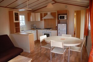 A compact kitchen with a dining area, including a microwave, stove, and refrigerator. - Camping 3 étoiles - Piscine  - ccbfeci (Penvénan)