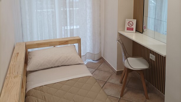 Een slaapkamer met een bed, een stoel, een bureau en een spiegel.