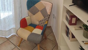 Een woonkamer met een kleurrijke fauteuil, een televisie op een dressoir en een boekenkast met boeken en een plant.