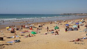 Ein Strand mit badenden Menschen, Sonnenschirmen und Zelten.