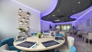 Ein moderner Essbereich mit runden Tischen, blauen Stühlen und einer Decke mit Sternenmuster.