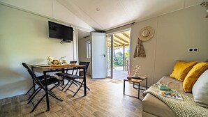 Ein Zimmer mit Esstisch, Stühlen, einer Couch, einem Fernseher und Blick durch eine Glastür.
