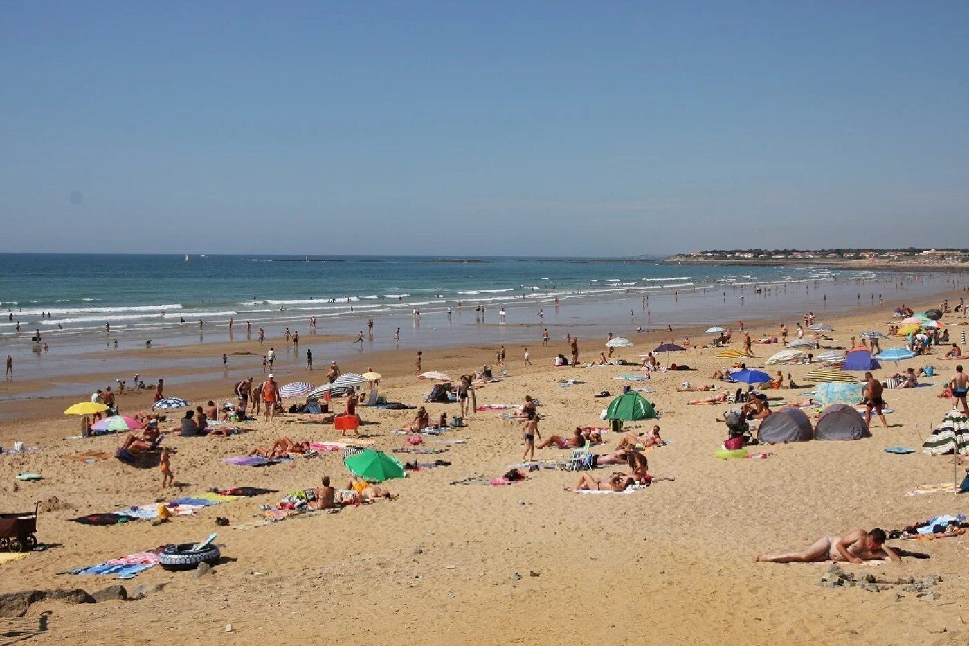 A beach with people sunbathing and swimming, tents, and umbrellas.