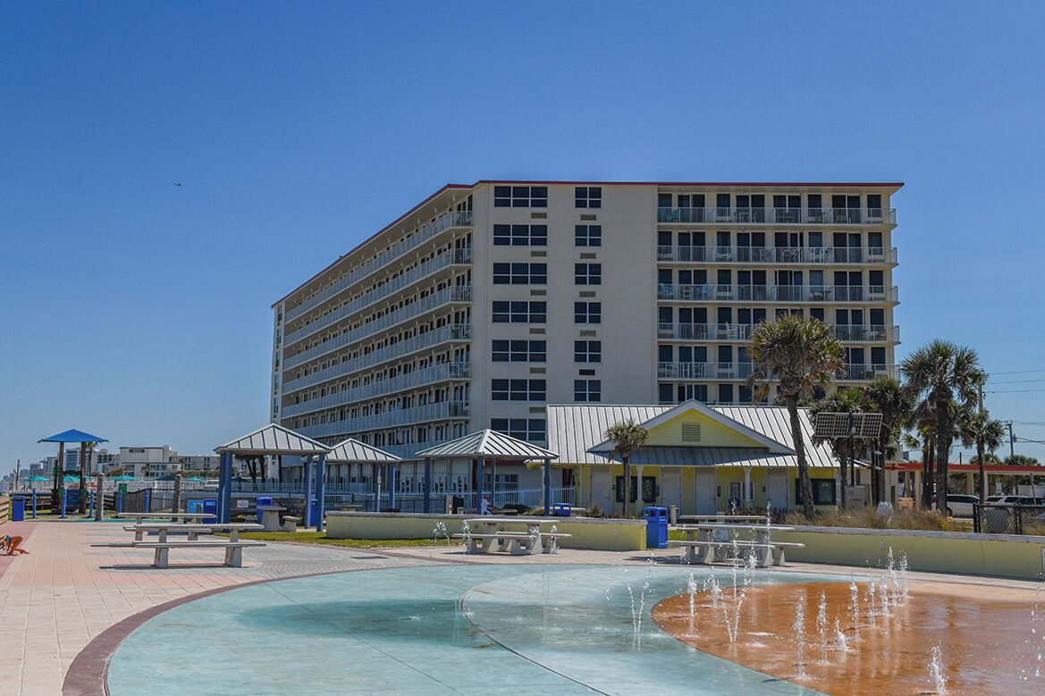Ein mehrstöckiges Hotel mit Balkonen, einem Pool mit Wasserspiel und Außenbereichen zum Sitzen.
