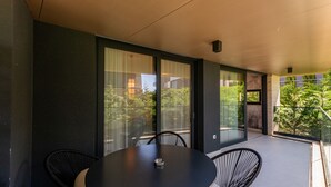Un área de comedor moderna al aire libre con una mesa redonda y sillas, puertas correderas de vidrio grandes y vistas a zonas verdes.