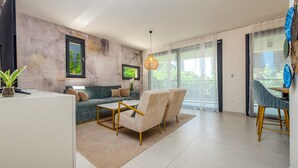 Una sala moderna con sofá, sillones, una mesa de centro, televisor y comedor con una silla.