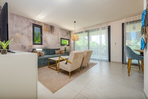 A modern living room with a sofa, armchairs, a coffee table, a TV, and a dining area with a chair. - Seaside Luxury Apartment Infinity Blue A2 (Zadar)