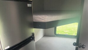 Interior d'una caravana domèstica amb petita cuina, lliteres i una finestra que ofereix vistes a l'exterior.