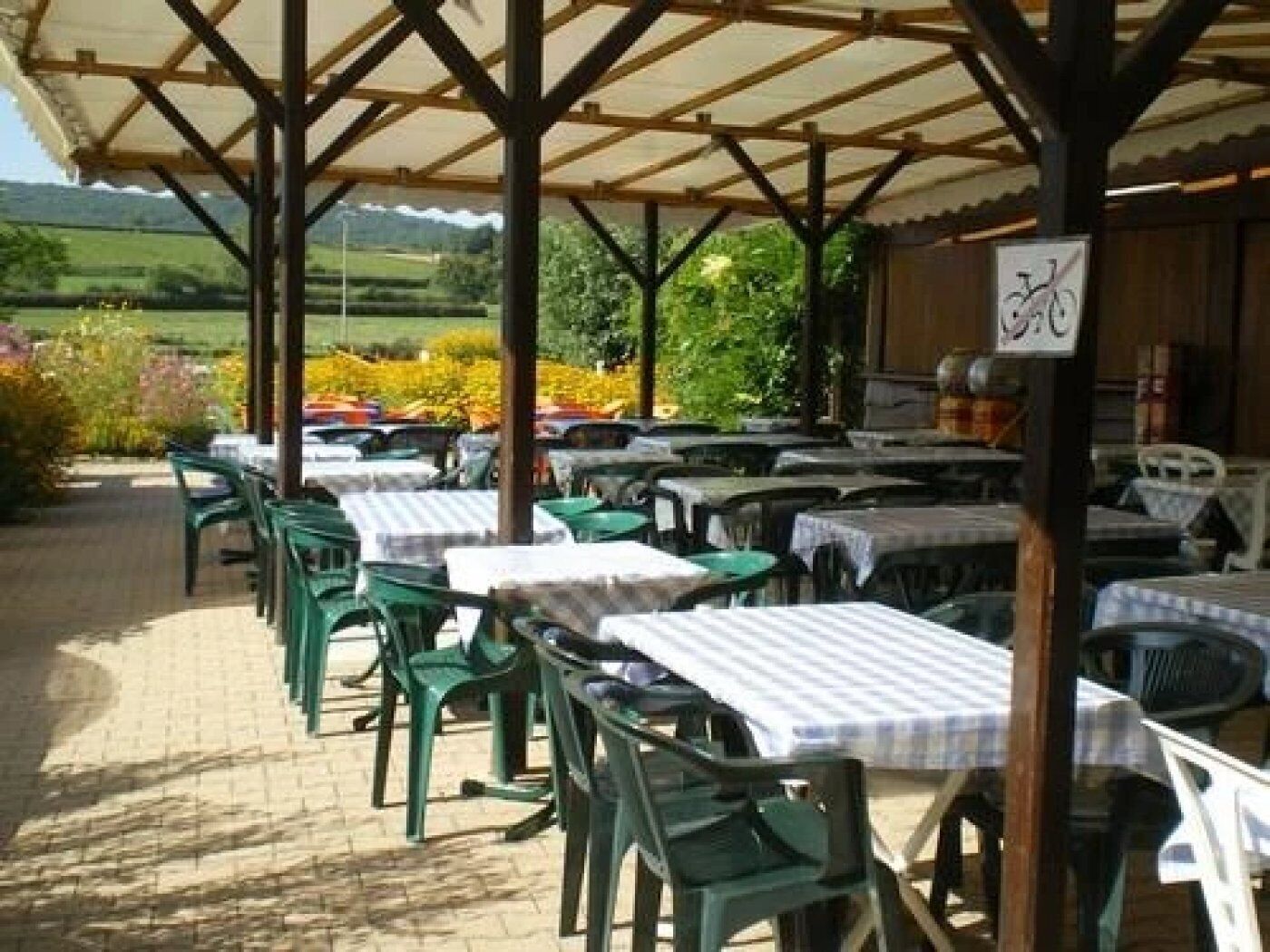 An outdoor patio with tables and chairs, a covered area, and a view of a green landscape.