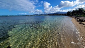 Una playa despejada con un arco de fútbol en el agua, una orilla arenosa y una costa distante con edificios y palmeras.