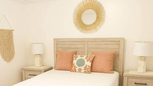 Una cama con cabecera de madera, dos mesitas de noche con lámparas, un colgador de macramé en la pared y un espejo redondo.