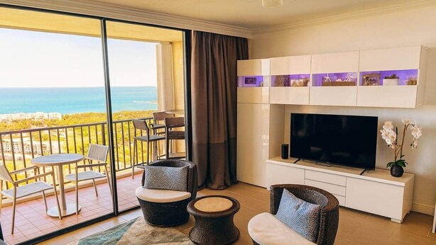 Un balcón con vista al océano, un televisor y muebles de mimbre.
