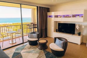 Un balcón con vista al océano, un televisor y muebles de mimbre.