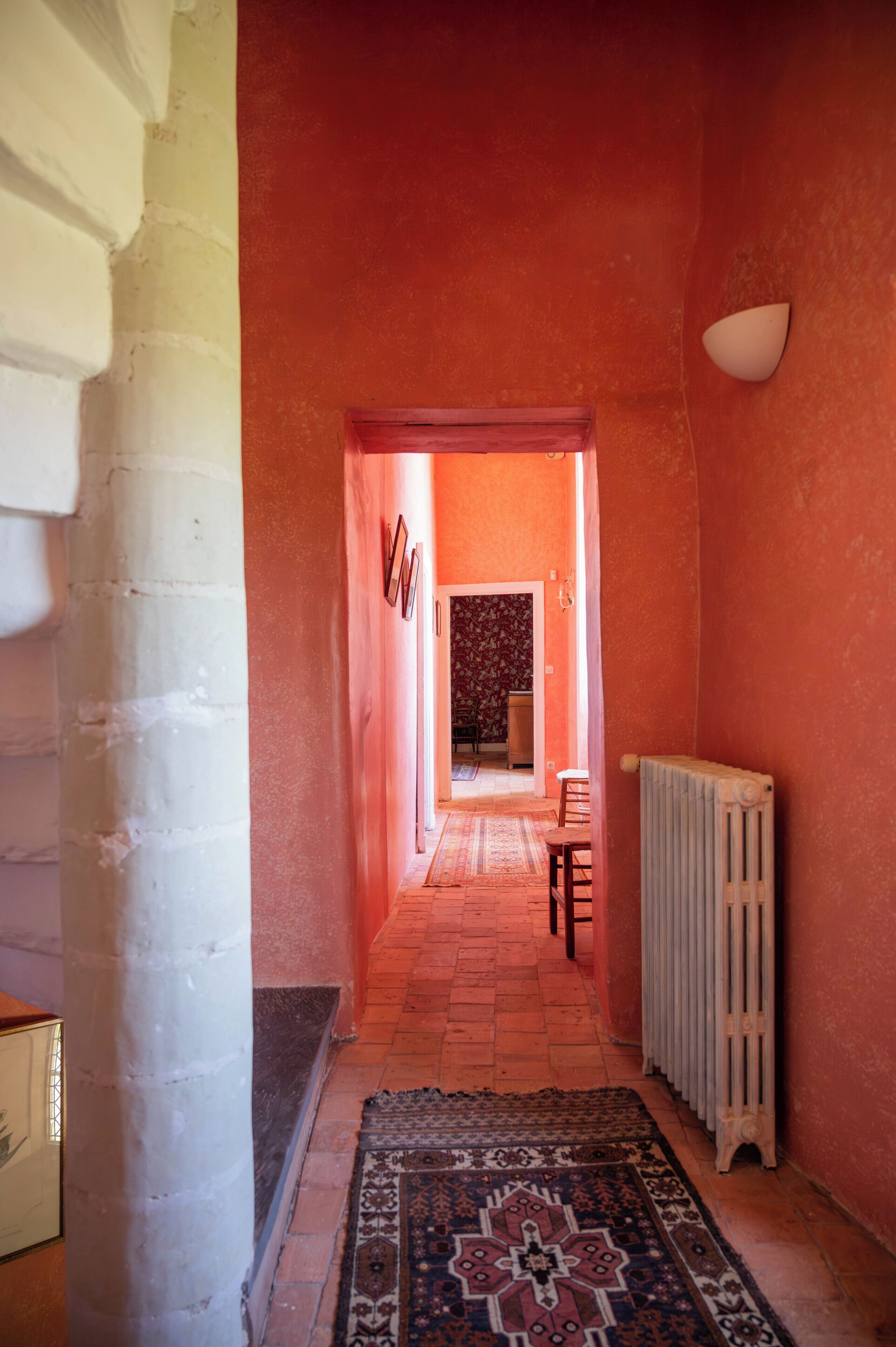 Un couloir avec un tapis à motifs, un radiateur et une chaise.